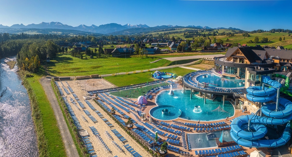Aerial view of Chochołowskie Thermal Baths featuring large outdoor blue pools, water slides, and panoramic views of the Tatra Mountains