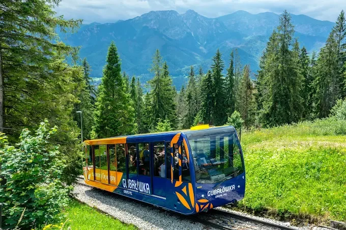 Blue and orange Gubalowka funicular travelling through a green summer landscape below the Tatra Mountains