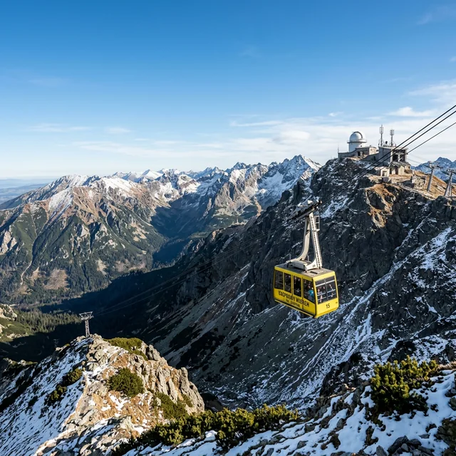 Yellow Kasprowy Wierch cable car crossing a snowy mountain slope below the summit station
